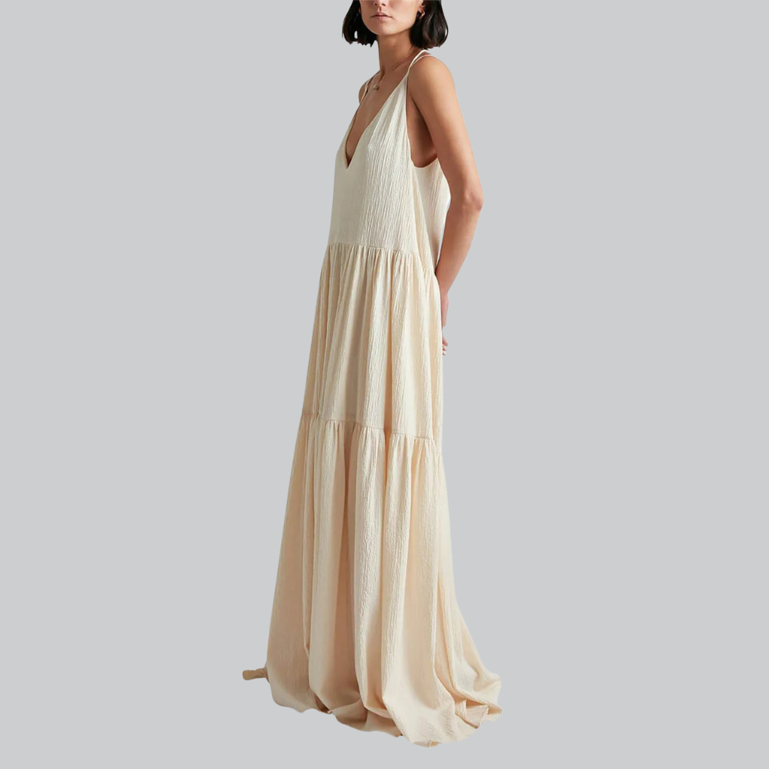 Frau in langem, ärmellosem, cremefarbenem Maxikleid mit V-Ausschnitt, seitlich stehend. Elegantes Sommerkleid, modisch, luftiger Stoff.