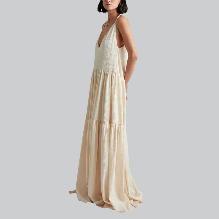 Frau in langem, ärmellosem, cremefarbenem Maxikleid mit V-Ausschnitt, seitlich stehend. Elegantes Sommerkleid, modisch, luftiger Stoff.
