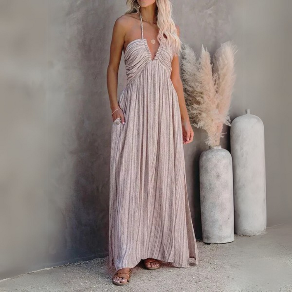Frau in langem, ärmellosem Sommerkleid vor grauer Wand, neben Pampasgras in Vasen. Elegantes, luftiges Outfit für warme Tage.