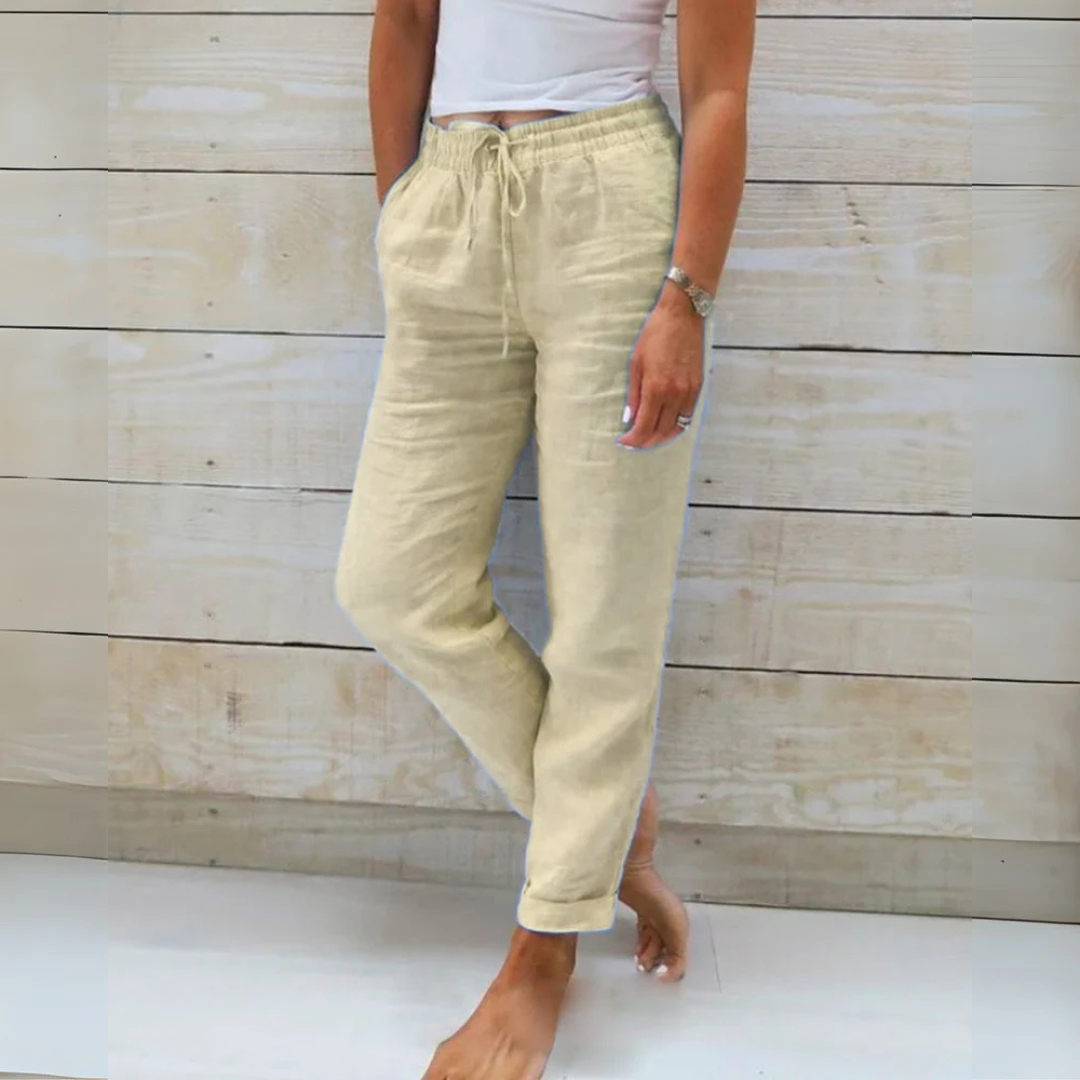 Damen in beiger Leinenhose und weißem Top vor Holzwand. Sommermode, lässiger Stil, bequeme Kleidung, Freizeitlook.