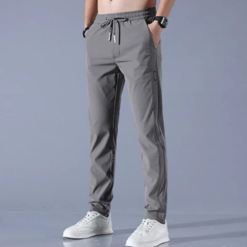 Graue Jogginghose für Herren, sportlich und bequem, mit Kordelzug und Taschen, kombiniert mit weißen Sneakers. Ideal für Freizeit und Sport.