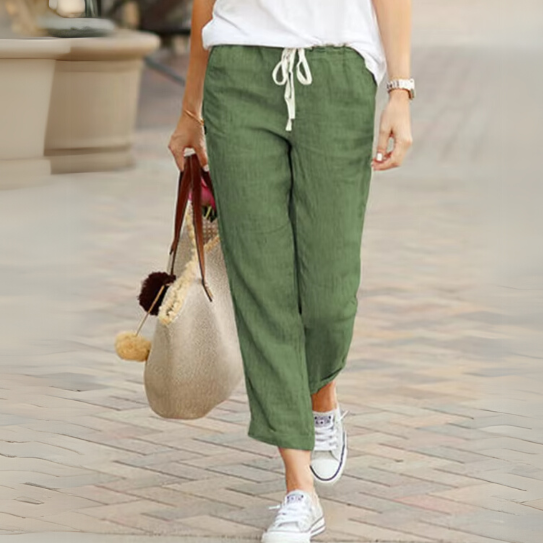 Frau in grüner Leinenhose und weißen Sneakers, trägt eine beige Tasche. Lässige Sommermode, bequeme Damenbekleidung, stilvoller Freizeitlook.