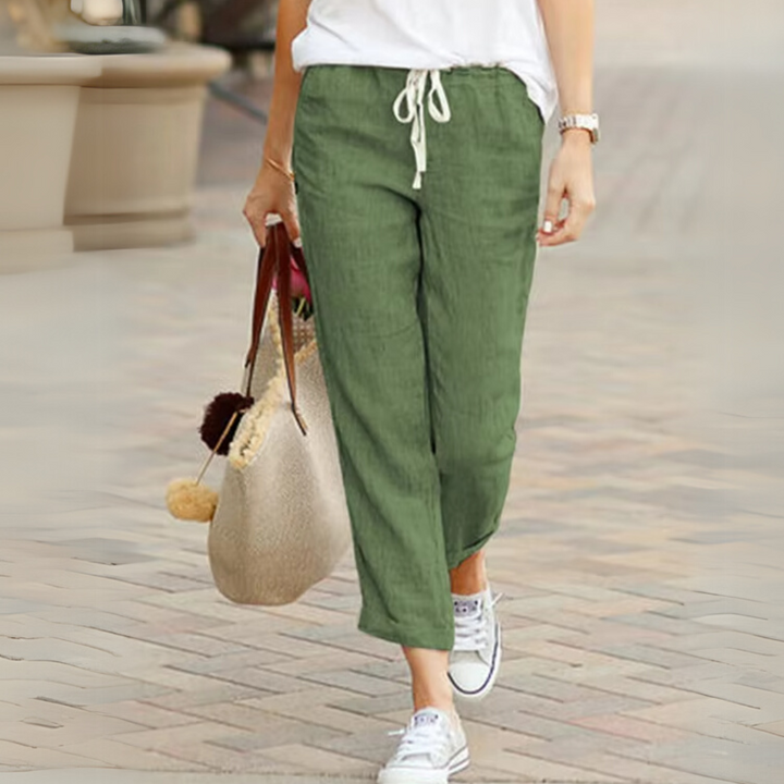 Frau in grüner Leinenhose und weißen Sneakers, trägt eine beige Tasche. Lässige Sommermode, bequeme Damenbekleidung, stilvoller Freizeitlook.