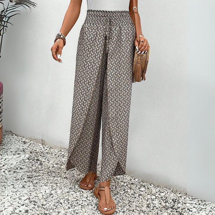 Frau in gemusterten Sommerhosen, Sandalen und mit Fransenhandtasche. Modetrend, Damenbekleidung, lässiger Stil, Sommermode.