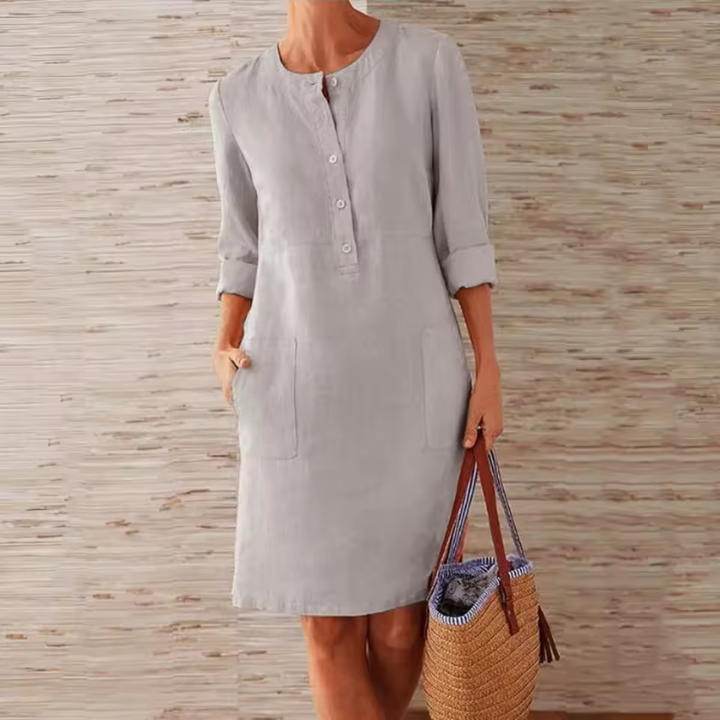 Dame in grauem Leinenkleid mit Knopfleiste, hält eine Strohtasche. Sommermode, Freizeitkleidung, elegantes Design, Damenbekleidung.