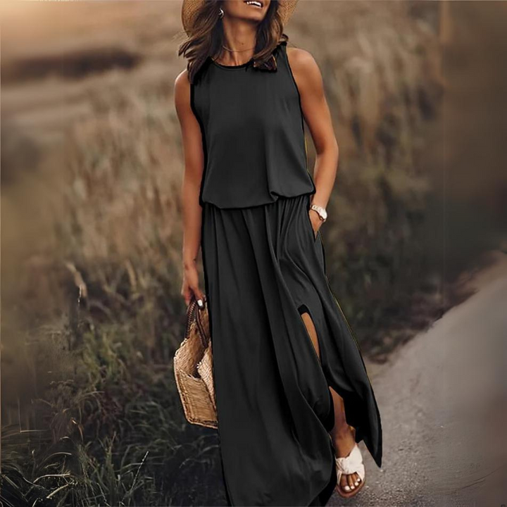Frau in schwarzem Maxikleid mit Strohhut und Korbtasche spaziert auf einem ländlichen Weg. Sommermode, elegantes Outfit, Freizeitkleidung.