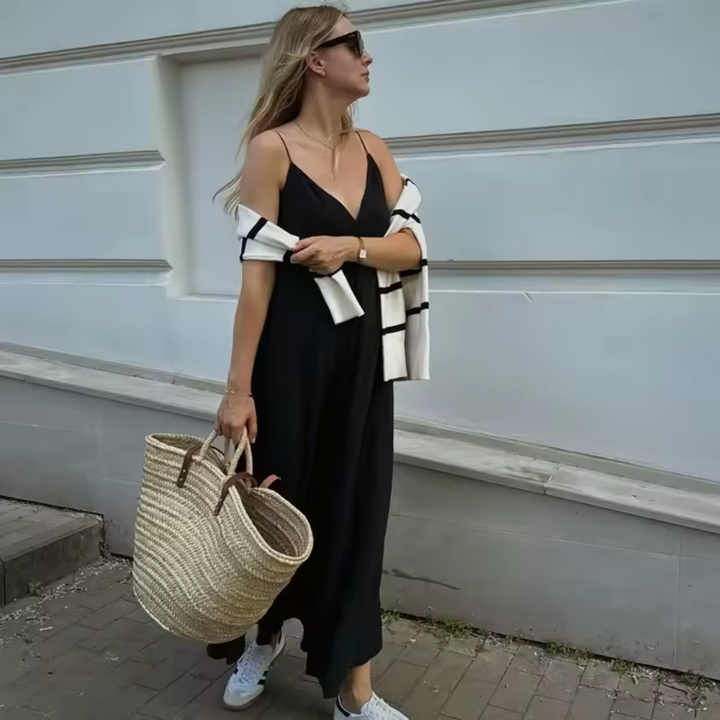 Frau in schwarzem Sommerkleid mit Strohtasche und Sonnenbrille vor weißer Wand. Modetrend, Sommeroutfit, lässiger Stil, Damenmode.