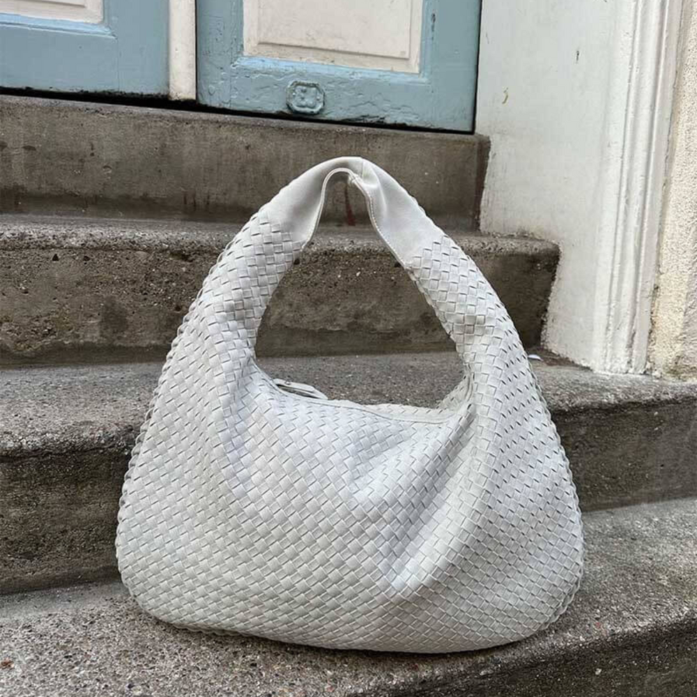 Weiße, geflochtene Handtasche auf Treppe vor blauer Tür. Modische Damenhandtasche, elegantes Design, Accessoire für stilvolle Outfits.