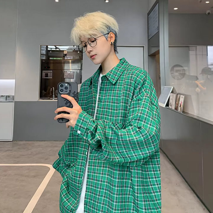 Junger Mann mit blonder Frisur und Brille macht Selfie in modernem Raum, trägt grün kariertes Hemd. Mode, Selfie, moderner Stil.