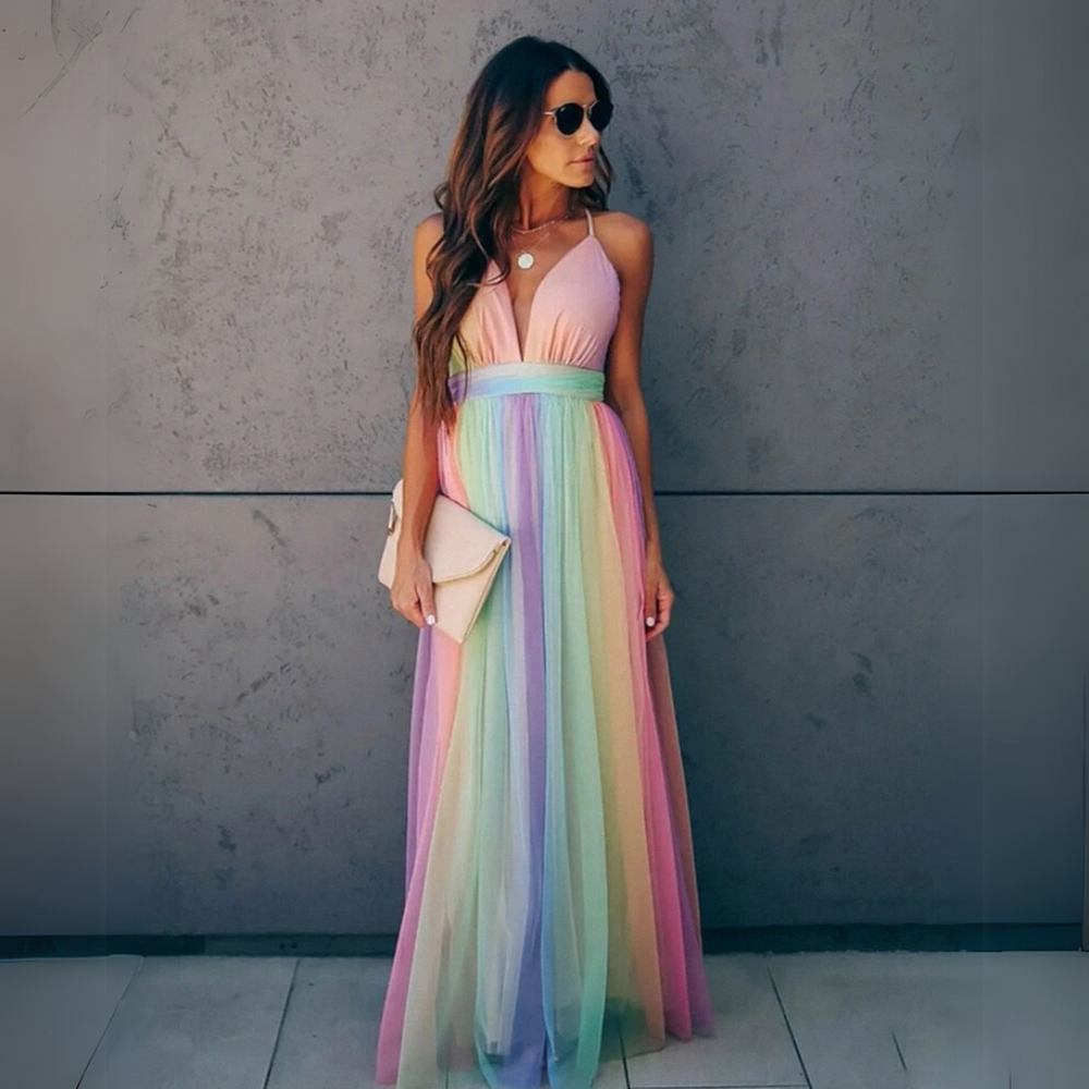 Frau in langem, ärmellosem Regenbogenkleid mit Sonnenbrille und Clutch vor grauer Wand. Elegantes Sommeroutfit, modisch, farbenfroh.