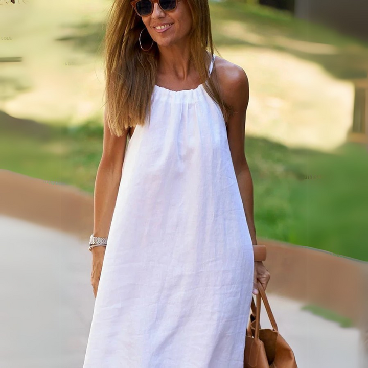 Frau in weißem Sommerkleid, Sonnenbrille, braune Tasche, lächelnd im Freien. Modetrend, Sommermode, lässiger Stil, Damenbekleidung.