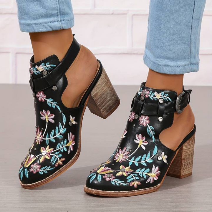 Schwarze Lederstiefeletten mit bunten Blumenstickereien, Blockabsatz und Schnallenverschluss, getragen mit hellblauen Jeans.