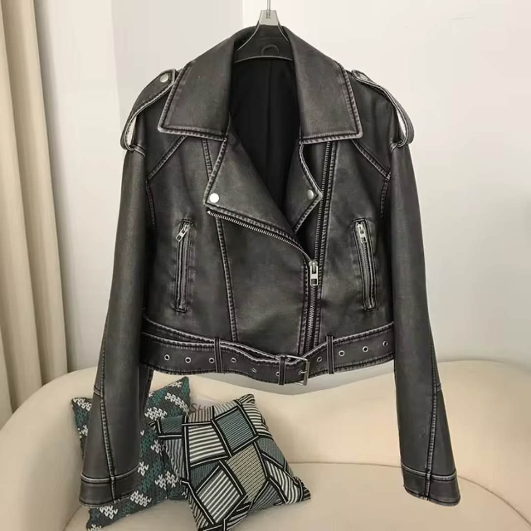 Schwarze Lederjacke mit Reißverschluss und Gürtel, hängend auf einem Kleiderbügel. Perfekt für Biker-Look und modische Outfits.