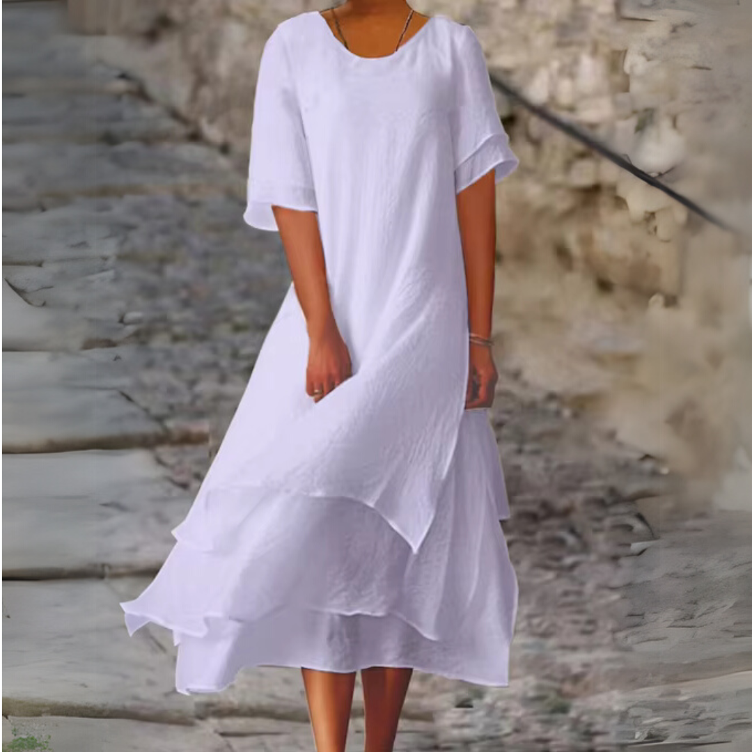 Frau in elegantem, weißem Sommerkleid auf Kopfsteinpflaster. Fließender Stoff, modisch, stilvoll. Perfekt für warme Tage und elegante Anlässe.