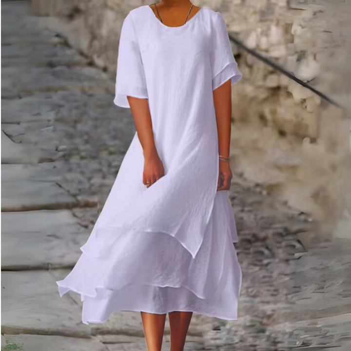 Frau in elegantem, weißem Sommerkleid auf Kopfsteinpflaster. Fließender Stoff, modisch, stilvoll. Perfekt für warme Tage und elegante Anlässe.