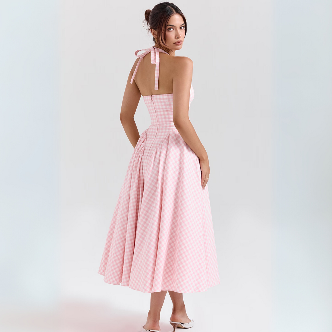 Frau in rosa kariertem Sommerkleid, rückenfrei, mit Schleife, steht auf weißem Hintergrund. Elegantes, modisches Design, ideal für Sommermode.