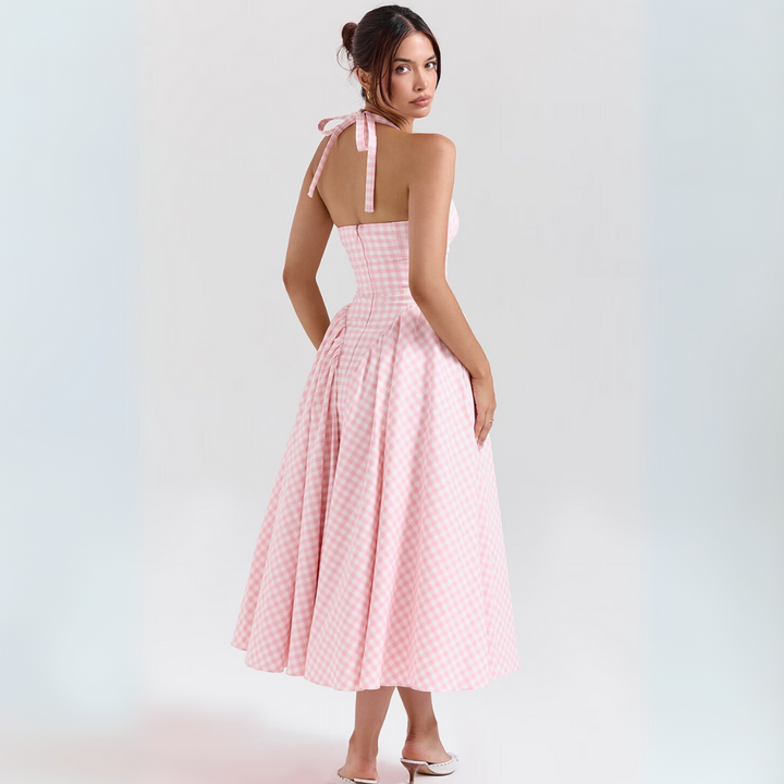 Frau in rosa kariertem Sommerkleid, rückenfrei, mit Schleife, steht auf weißem Hintergrund. Elegantes, modisches Design, ideal für Sommermode.