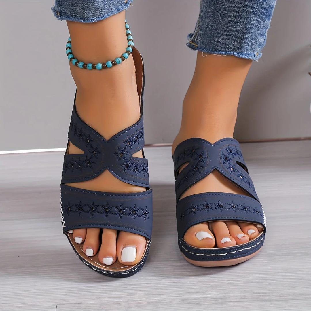 Blaue Sandalen mit Stickerei, getragen von einer Person mit Jeans und türkisfarbenem Fußkettchen. Modische Sommerschuhe für Damen.