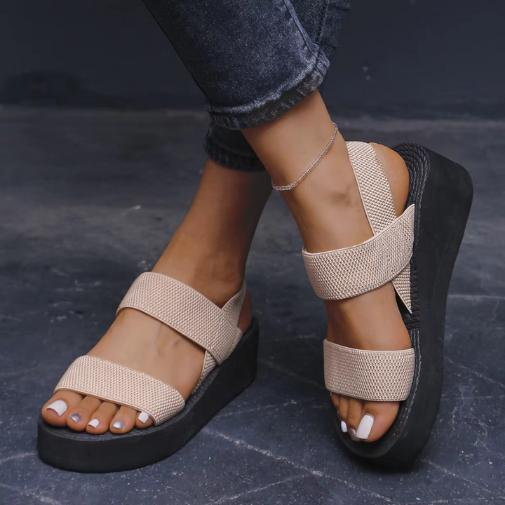 Beige Plateau-Sandalen mit breiten Riemen an Frauenfüßen, kombiniert mit dunklen Jeans. Modische Sommerschuhe, bequem und stilvoll.