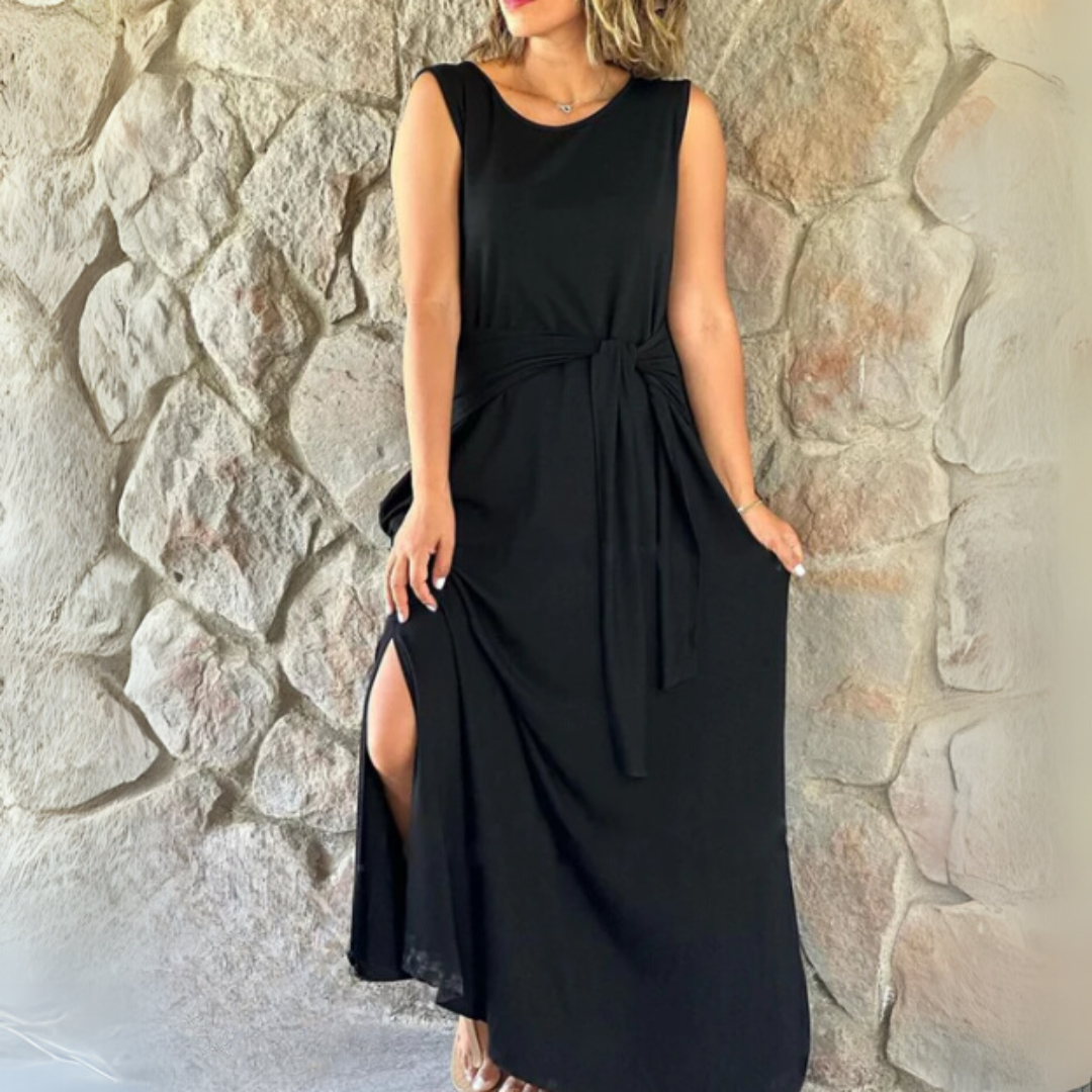 Frau in elegantem, schwarzem Maxikleid mit seitlichem Schlitz vor Steinwand. Sommermode, Abendkleid, stilvolle Damenbekleidung.