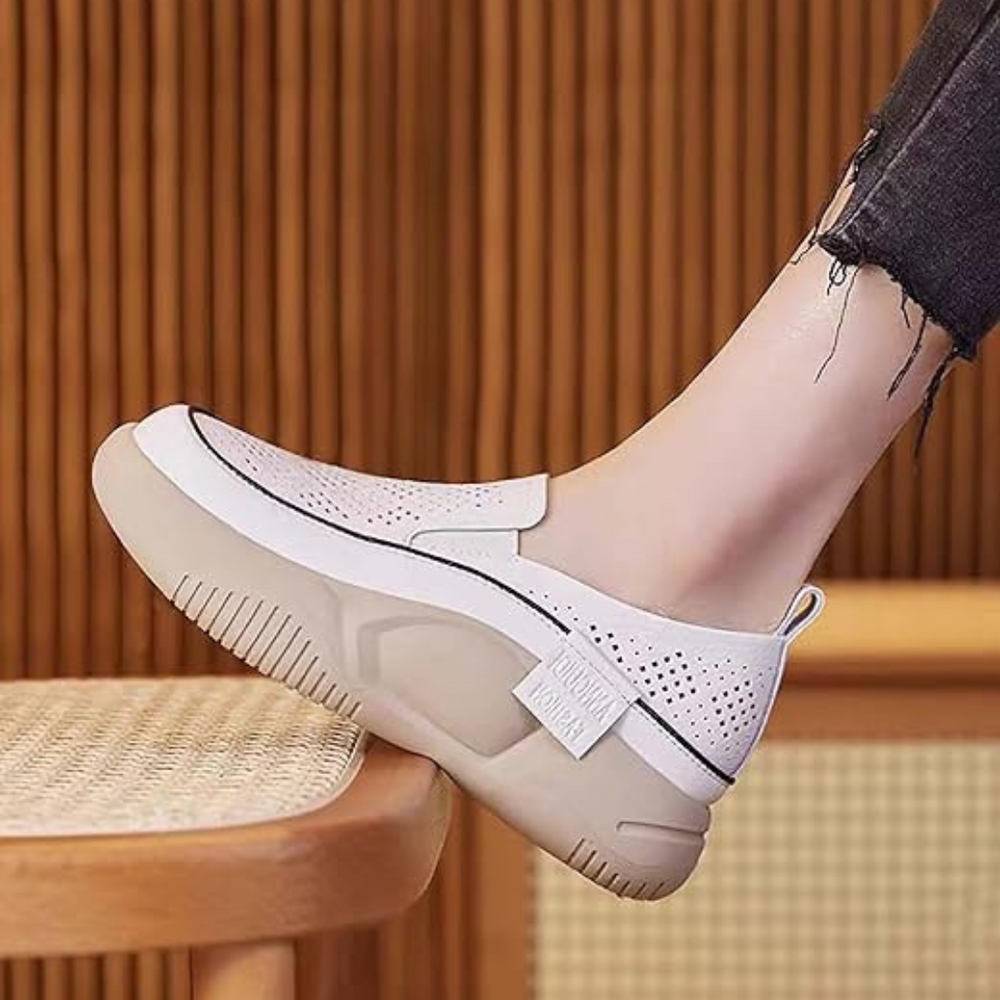 Weiße Damen-Sneaker mit dicker Sohle, perforiertem Design und modernem Look, getragen mit schwarzer Jeans. Ideal für trendige Freizeitmode.