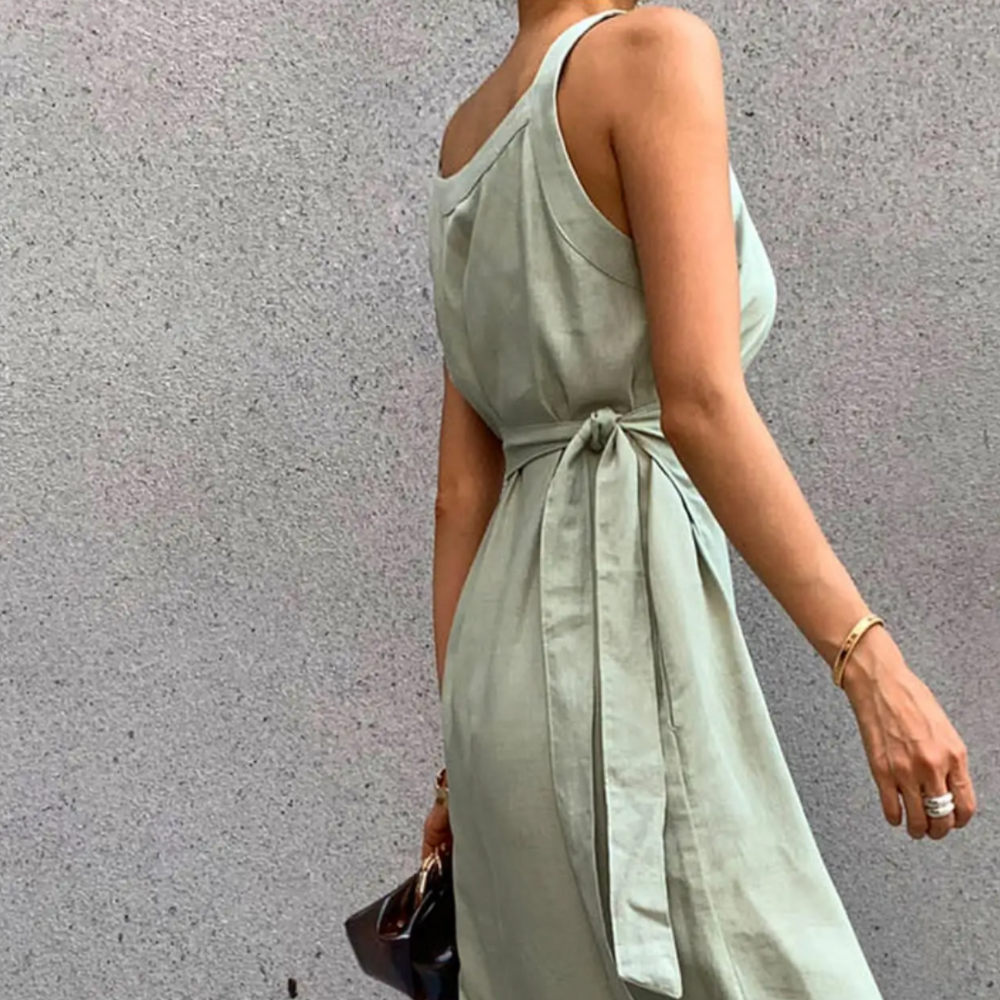 Frau in elegantem, ärmellosem, hellgrünem Kleid mit Gürtel, hält eine braune Tasche. Perfekt für Sommermode und stilvolle Outfits.