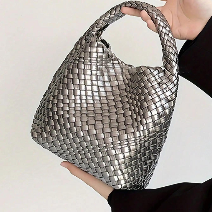 Silberne, geflochtene Handtasche in Dreiecksform, gehalten von einer Hand. Modische Damenaccessoire, elegant und stilvoll für besondere Anlässe.