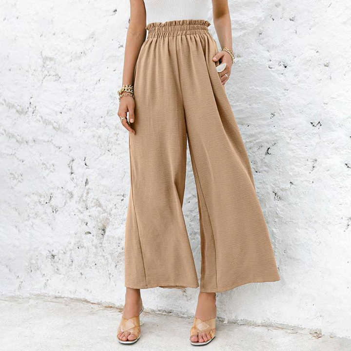 Frau in beige, weit geschnittener Hose vor weißer Wand. Modetrend, Sommeroutfit, Damenbekleidung, lässiger Stil, bequeme Hosen.