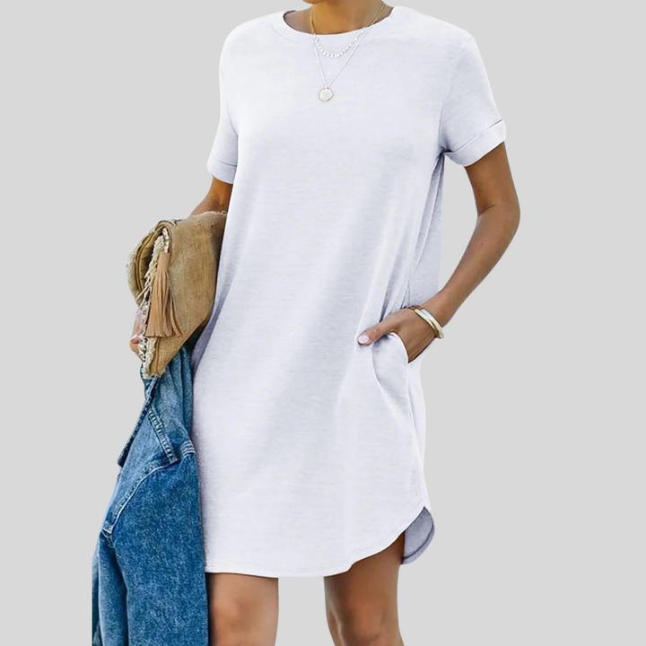 Frau in weißem T-Shirt-Kleid mit Taschen, hält braune Tasche und blaue Jeansjacke. Modetrend, lässiger Sommerlook, Damenbekleidung.