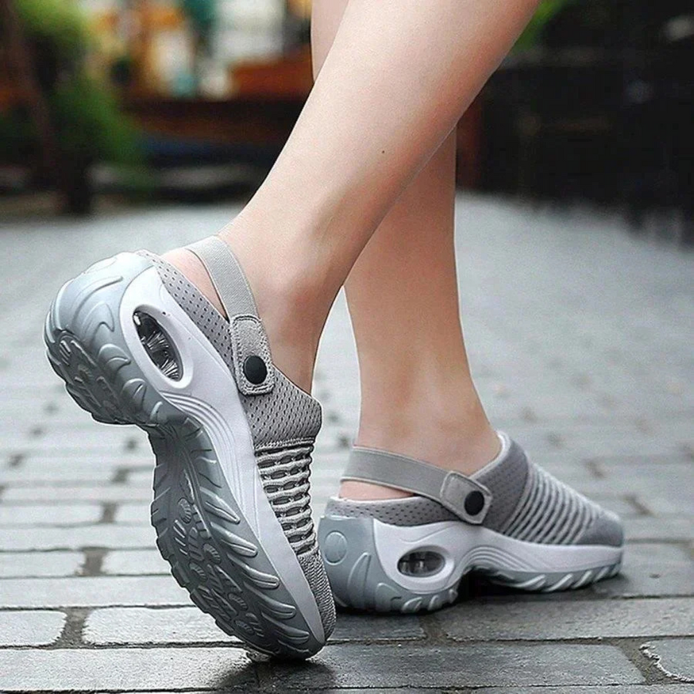 Graue, atmungsaktive Clogs mit rutschfester Sohle auf Kopfsteinpflaster. Bequeme, modische Schuhe für Damen, ideal für Freizeit und Outdoor.