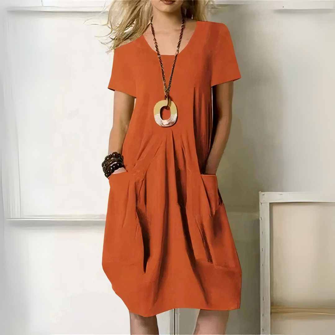 Frau in lockerem, orangefarbenem Sommerkleid mit Taschen und großem Anhänger. Modetrend, lässiger Stil, Damenmode, Sommeroutfit.