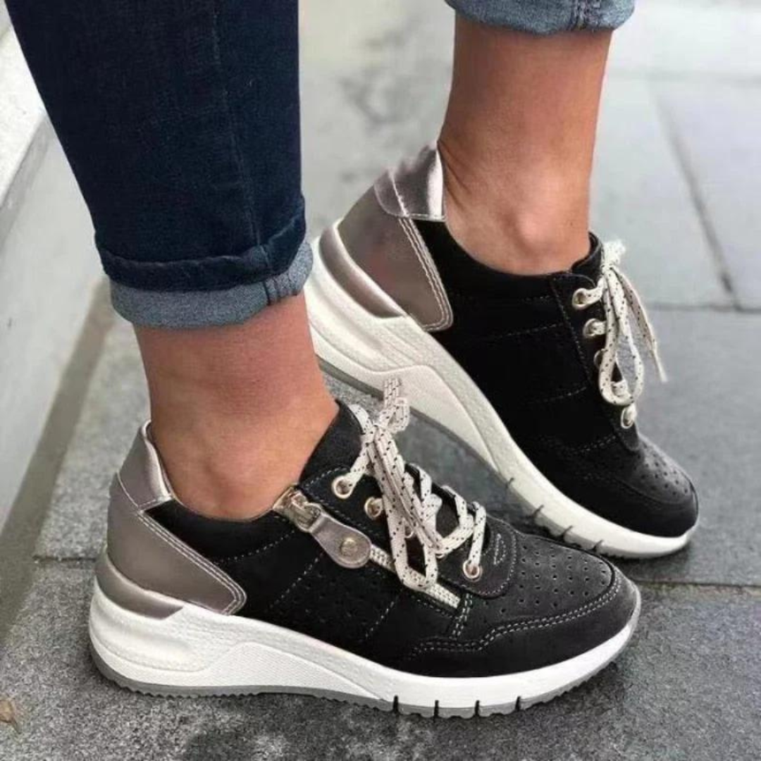 Schwarze Damen-Sneaker mit weißer Sohle und silbernen Details, getragen von Person in Jeans. Modische Freizeitschuhe, ideal für den Alltag.