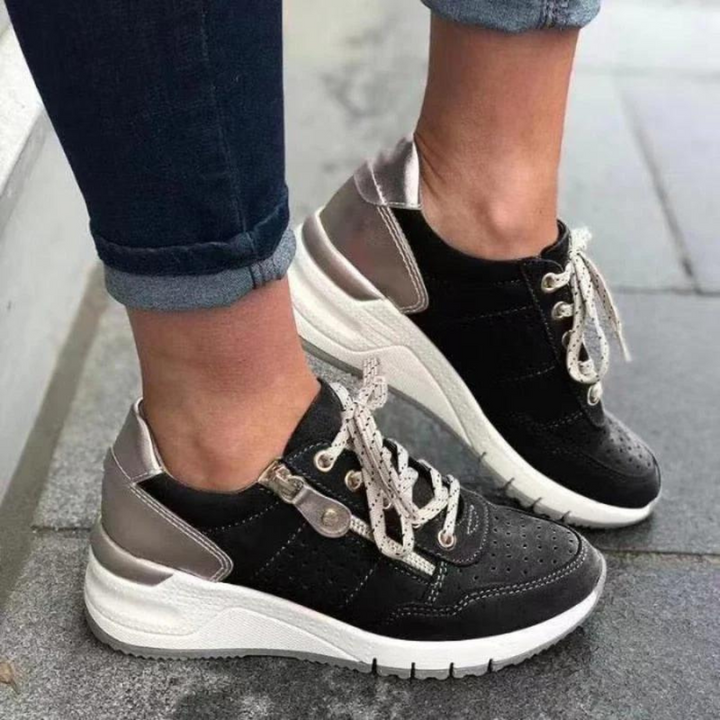 Schwarze Damen-Sneaker mit weißer Sohle und silbernen Details, getragen von Person in Jeans. Modische Freizeitschuhe, ideal für den Alltag.