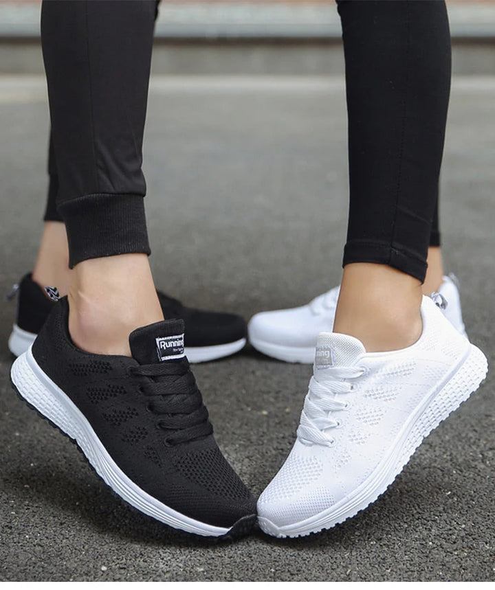 Zwei Paar Sportschuhe, schwarz und weiß, auf Asphalt getragen von Personen in schwarzen Leggings. Bequeme, atmungsaktive Laufschuhe für Damen.