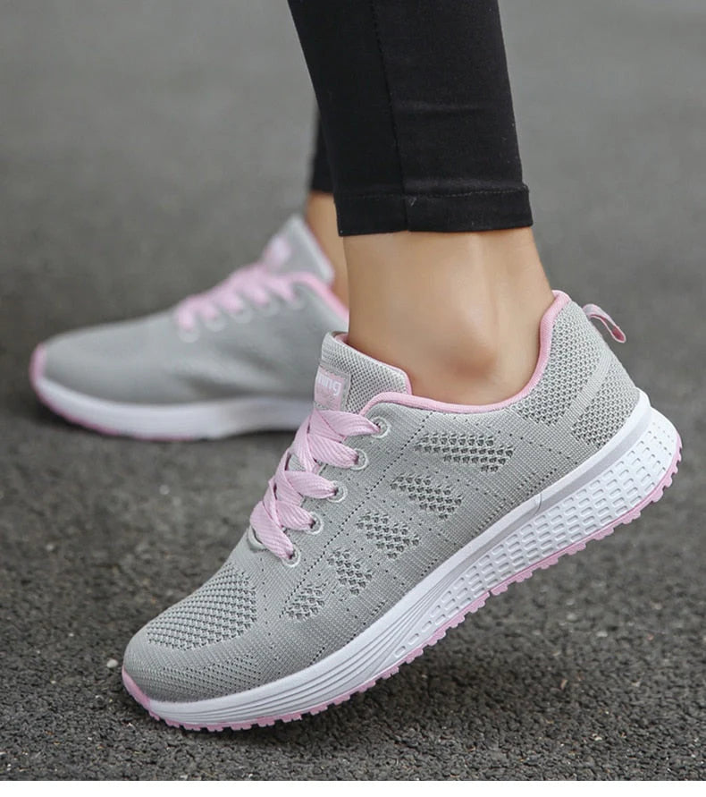 Graue Damen-Sneaker mit rosa Schnürsenkeln, atmungsaktives Mesh-Design, ideal für Laufen und Freizeit, auf Asphalt getragen.