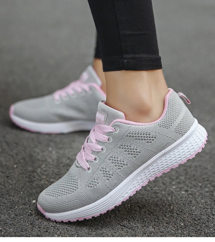 Graue Damen-Sneaker mit rosa Schnürsenkeln, atmungsaktives Mesh-Design, ideal für Laufen und Freizeit, auf Asphalt getragen.