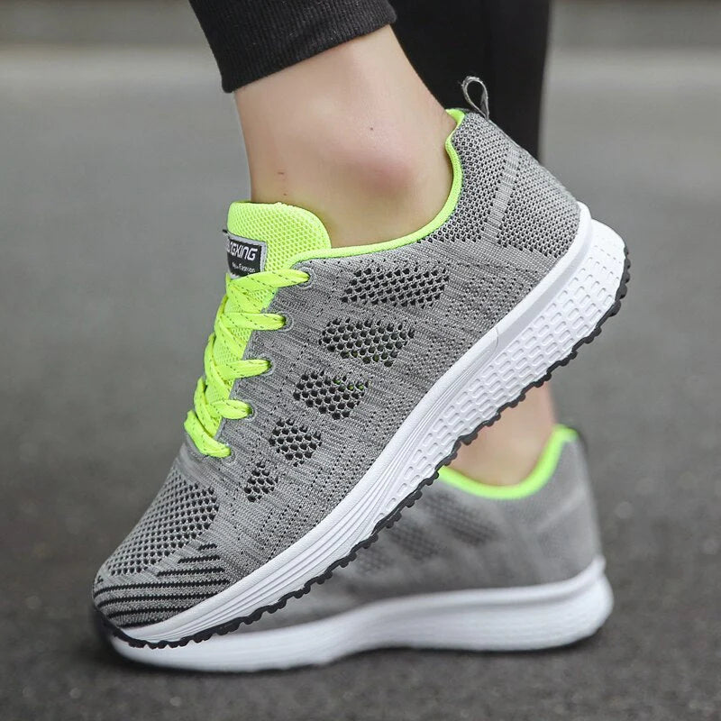 Graue Sportschuhe mit neongelben Schnürsenkeln und atmungsaktivem Mesh-Obermaterial auf Asphalt. Ideal für Laufen und Fitness.