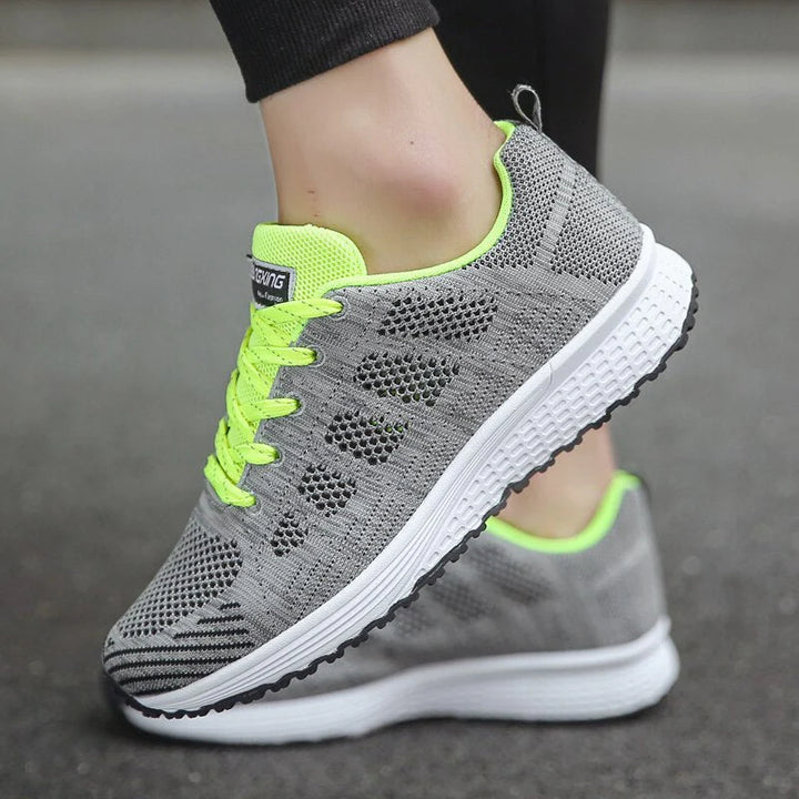 Graue Sportschuhe mit neongelben Schnürsenkeln und atmungsaktivem Mesh-Obermaterial auf Asphalt. Ideal für Laufen und Fitness.