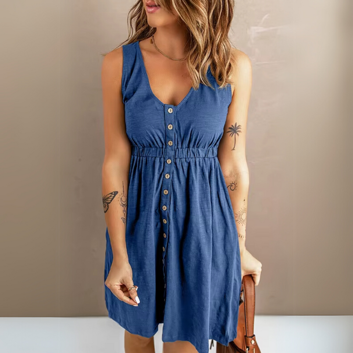 Frau in blauem Sommerkleid mit Knopfleiste, ärmellos, Tattoos auf Armen, hält braune Tasche. Modetrend, Damenbekleidung, Freizeitlook.