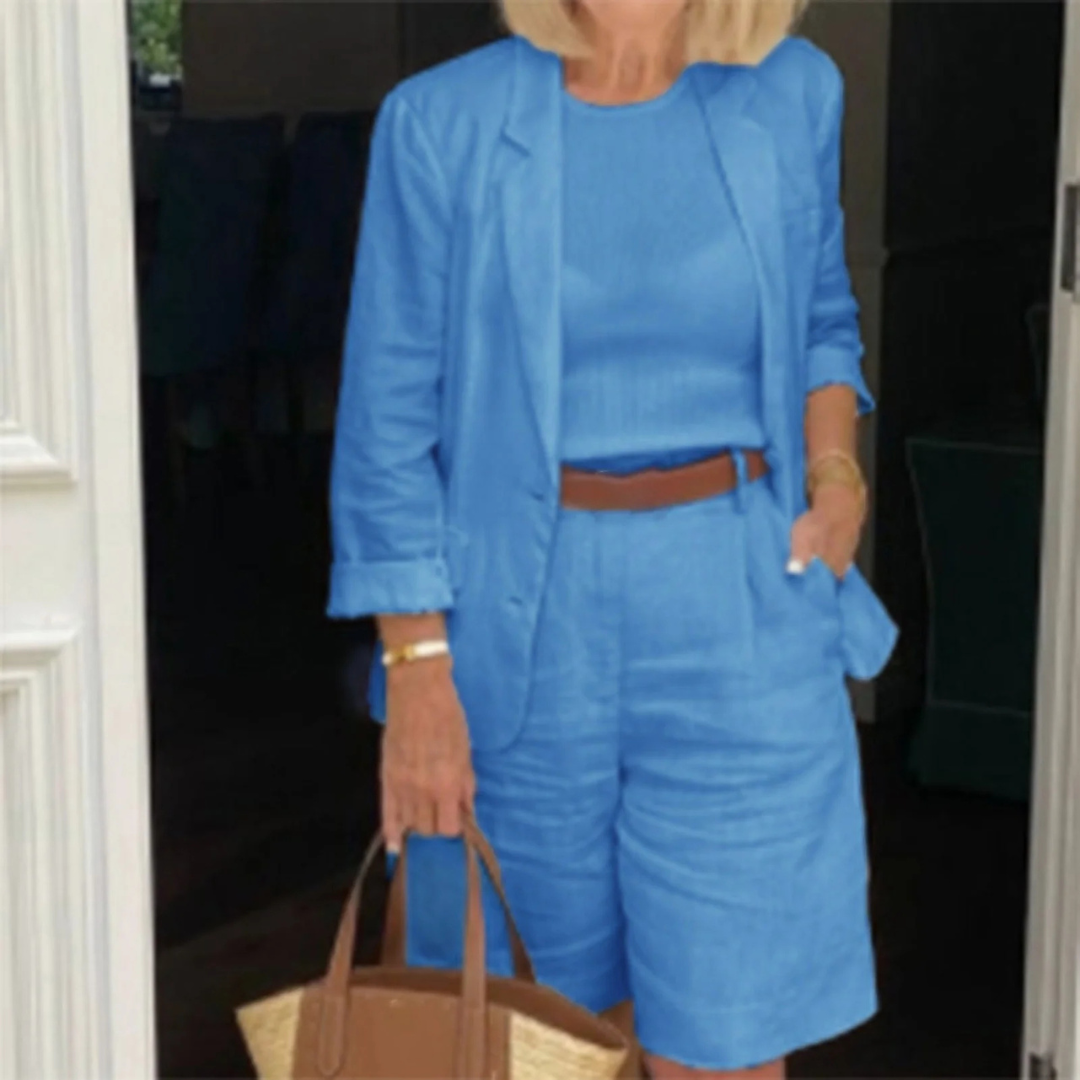 Frau in blauem Leinenanzug mit Shorts und Blazer, brauner Gürtel, Strohtasche, Sommermode, eleganter Freizeitlook, stilvoll gekleidet.