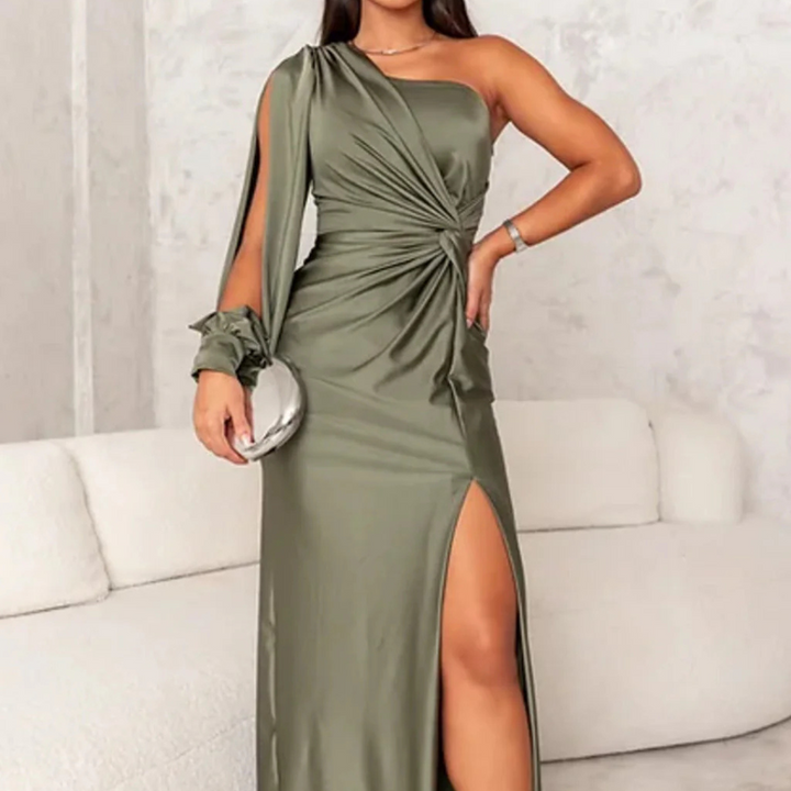 Grünes, schulterfreies Abendkleid mit hohem Beinschlitz, elegantes Design, Frau auf weißem Sofa, modisches Outfit für besondere Anlässe.