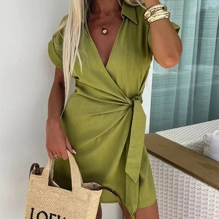 Frau in grünem Wickelkleid mit V-Ausschnitt, goldenen Armreifen und Strohtasche. Sommermode, elegantes Outfit, stilvolle Damenbekleidung.