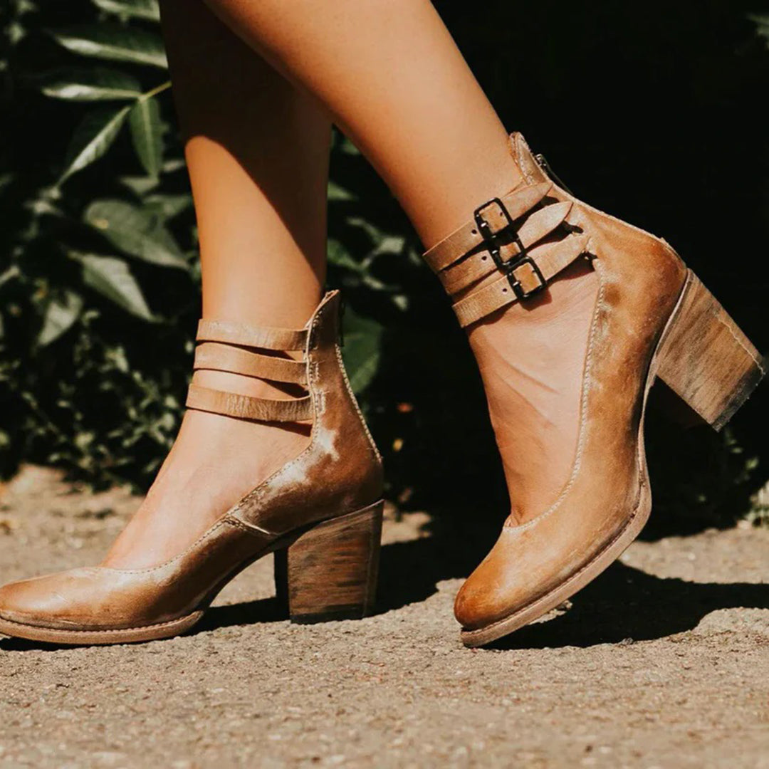 Braune Damenstiefeletten mit Blockabsatz und Schnallen, stilvoll auf einem sonnigen Gehweg präsentiert. Modische Schuhe für Herbst und Winter.