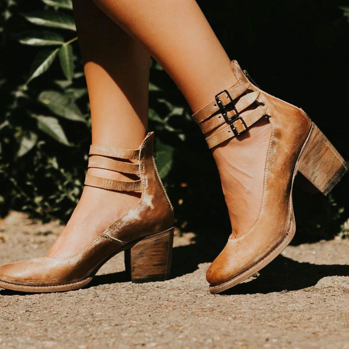 Braune Damenstiefeletten mit Blockabsatz und Schnallen, stilvoll auf einem sonnigen Gehweg präsentiert. Modische Schuhe für Herbst und Winter.