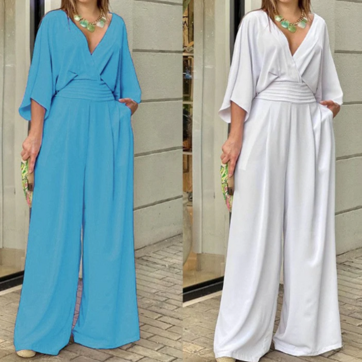 Zwei Frauen in eleganten Jumpsuits, einer in Blau, der andere in Weiß, mit weitem Bein und V-Ausschnitt, posieren vor einem Geschäft.
