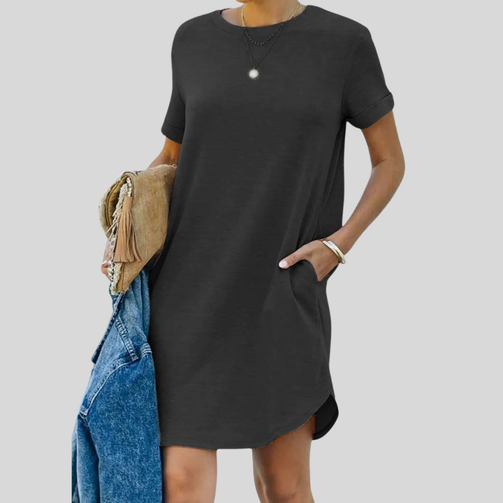 Frau in schwarzem T-Shirt-Kleid mit Taschen, hält Jeansjacke und Tasche. Modetrend, lässiger Stil, Sommeroutfit.