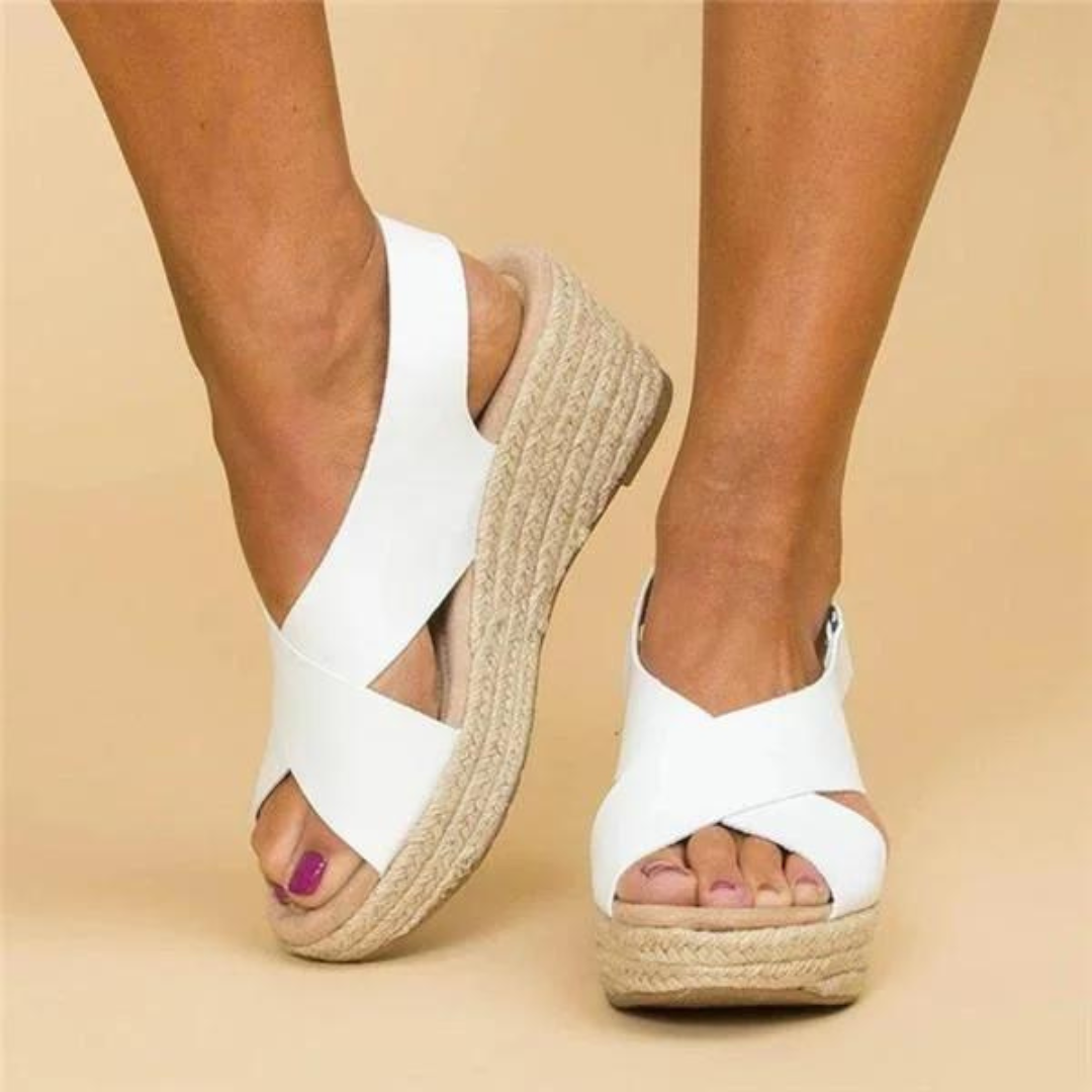 Weiße Keilsandalen mit Bastsohle an Frauenfüßen auf beigem Hintergrund. Modische Sommerschuhe, bequem und stilvoll für Damen.