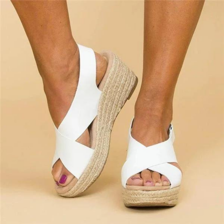Weiße Keilsandalen mit Bastsohle an Frauenfüßen auf beigem Hintergrund. Modische Sommerschuhe, bequem und stilvoll für Damen.