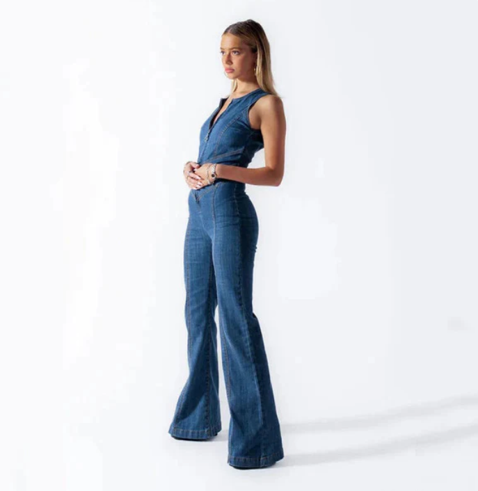 Frau in blauem Denim-Jumpsuit, stehend vor weißem Hintergrund. Modetrend, Damenmode, Jeans-Overall, eleganter Look, Freizeitkleidung.