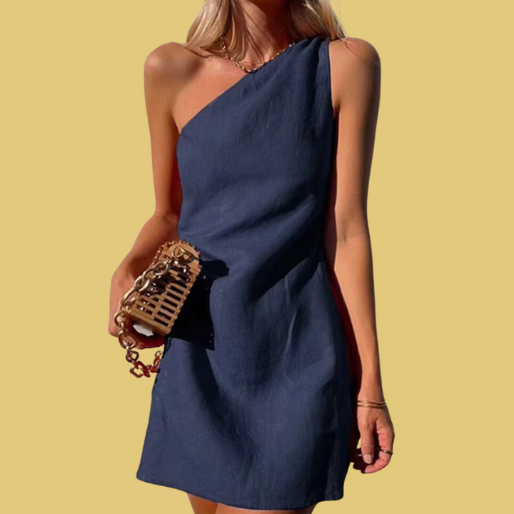Frau in einem eleganten, einseitigen blauen Kleid mit einer kleinen, stilvollen Handtasche vor gelbem Hintergrund. Sommermode, Damenkleid.